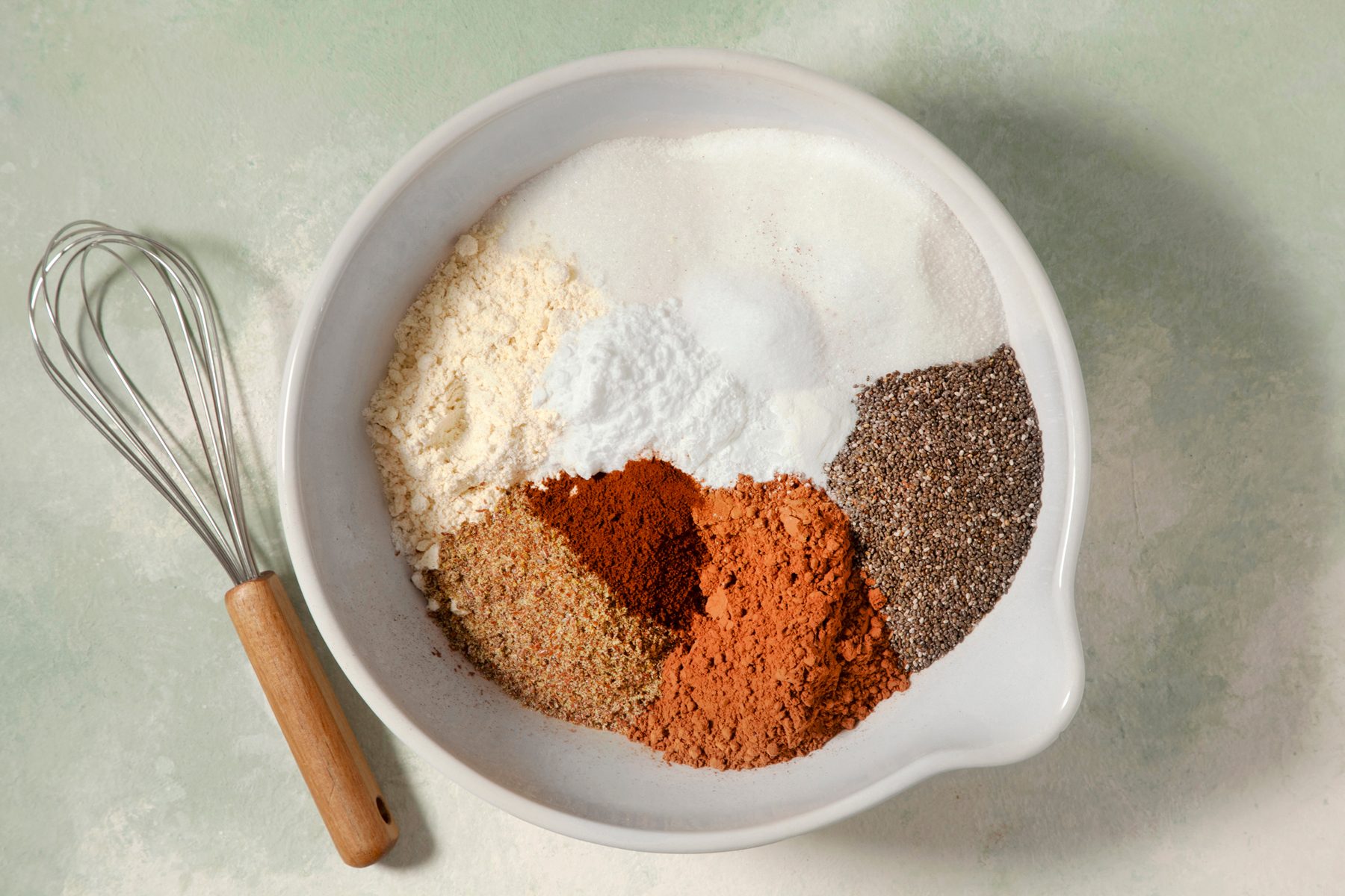 overhead shot; light green textured background; In a large bowl, placed flour and next 9 dry ingredients; whisker placed next to the bowl