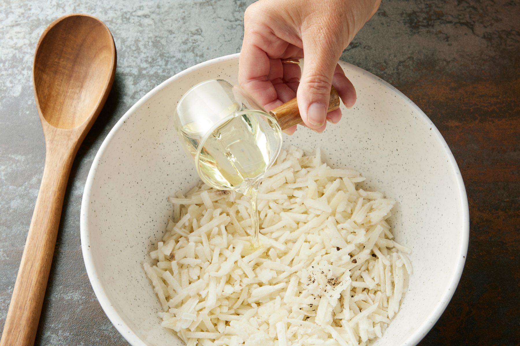 High angel view shot of a large bowl combine potatoes; oil and pepper; wooden spoon; dark texture surface