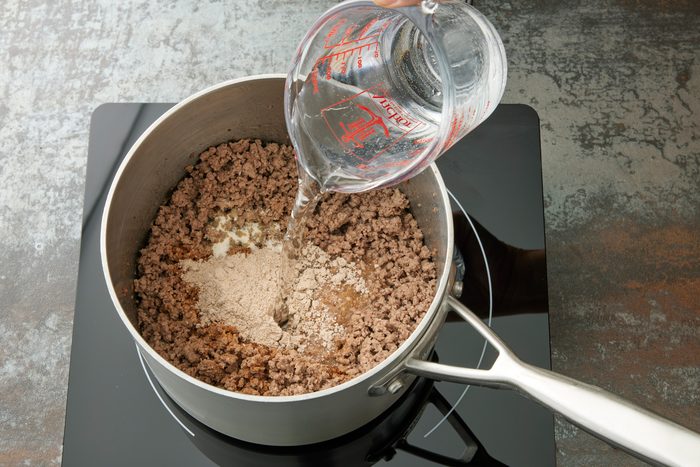 High angle view shot of the same saucepan; stir in water; gravy mix and garlic salt; bring to a boil; induction; dark texture surface