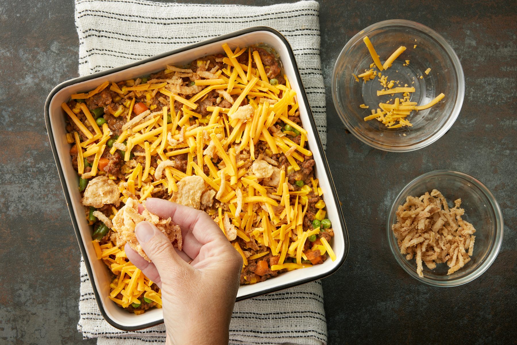 Overhead shot of baking pan; sprinkle with remaining onions and cheese; bake until cheese is melted; 5 minutes longer; kutchen towel; dark texture surface;