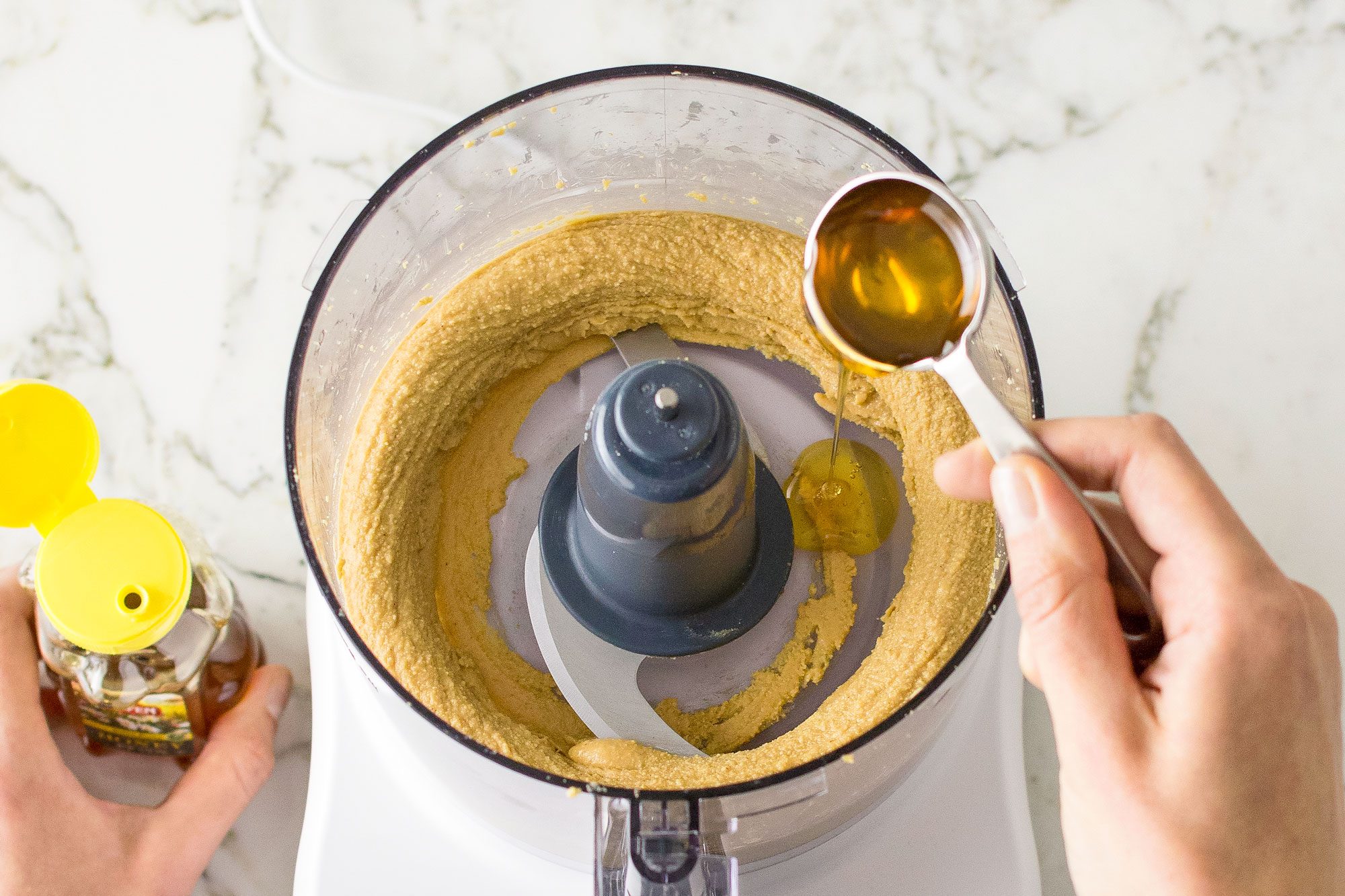 adding honey into a food processor; marble background;