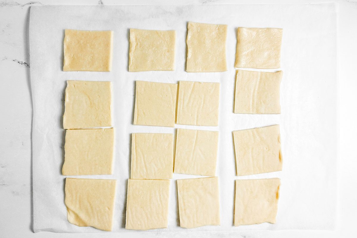 Squares of dough for Taste of Home Kolacky Cookies on a piece of parchment on a marble surface