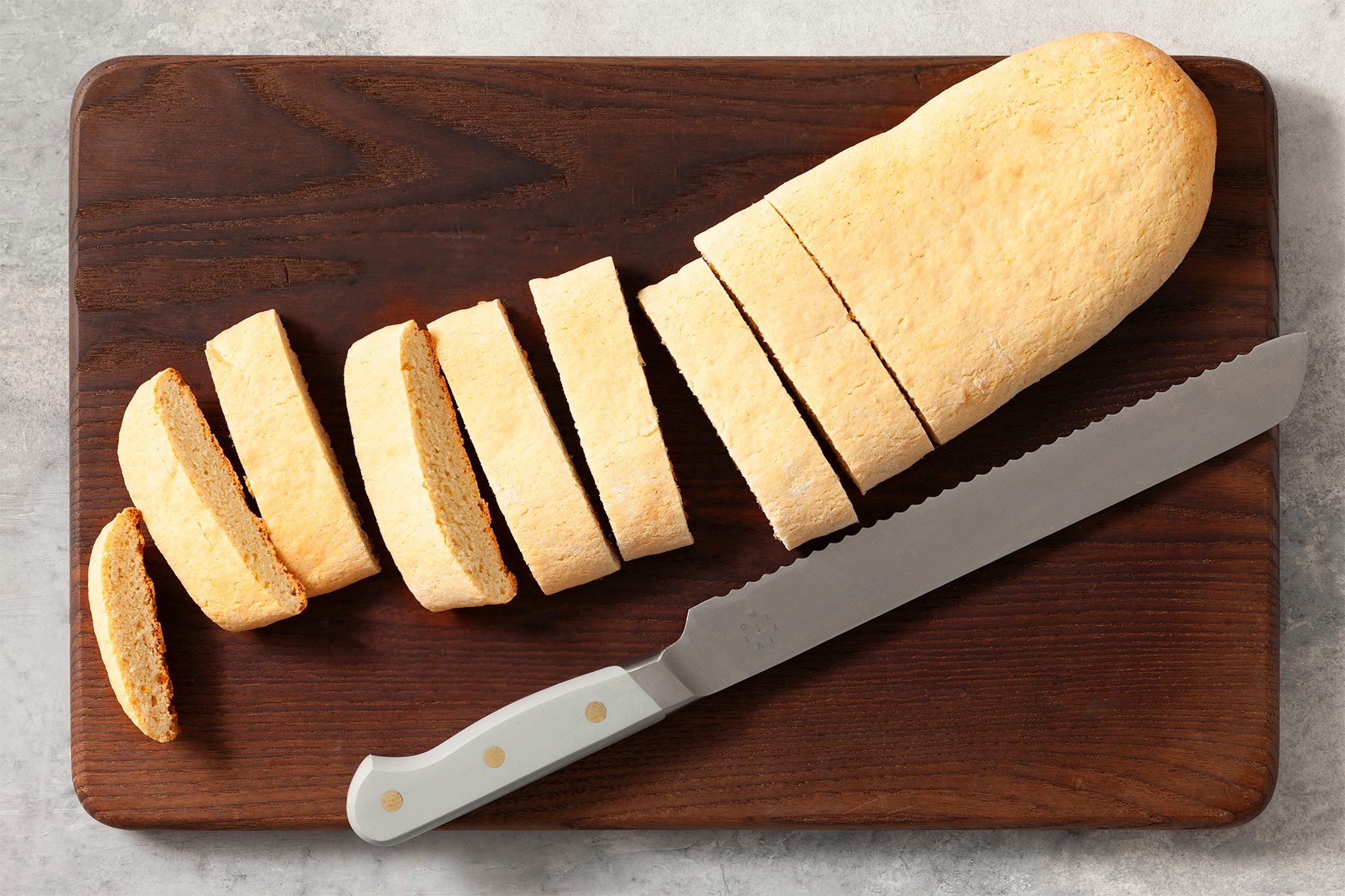 Overhead shot; carefully remove to wire racks; cool for 5 minutes; transfer to a cutting board; cut with a serrated knife into scant 3/4 inch slices; knife; grey marble surface;