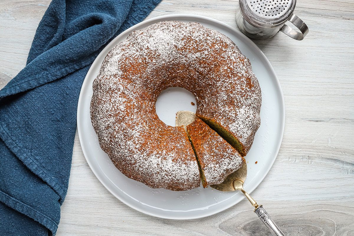 Overhead view of a lemon poppy seed cake with a slice being removed.