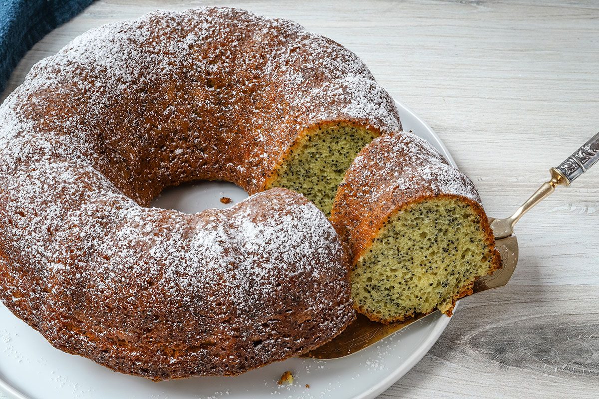 A slice is removed from a lemon poppy seed cake.