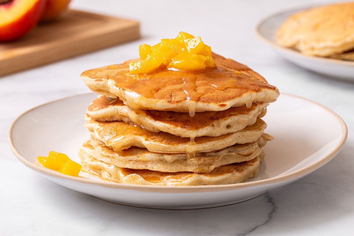 Peach Pancakes on a plate with butter syrup and topped with chopped peaches