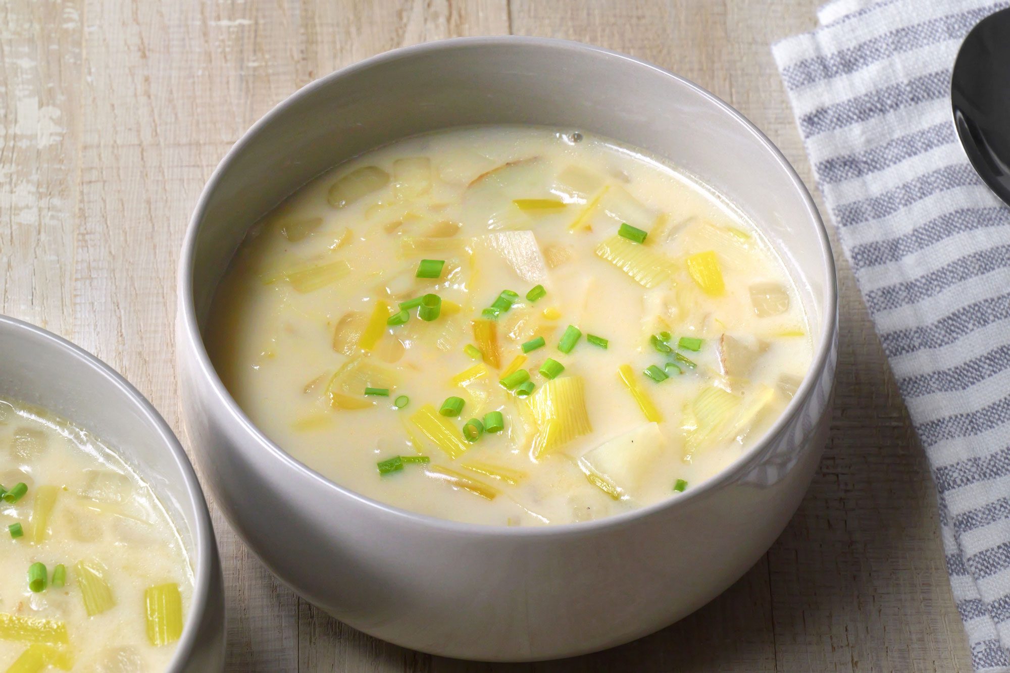 3/4th shot; wooden background; A bowl of creamy Potato Leek Soup is the centerpiece of the image;