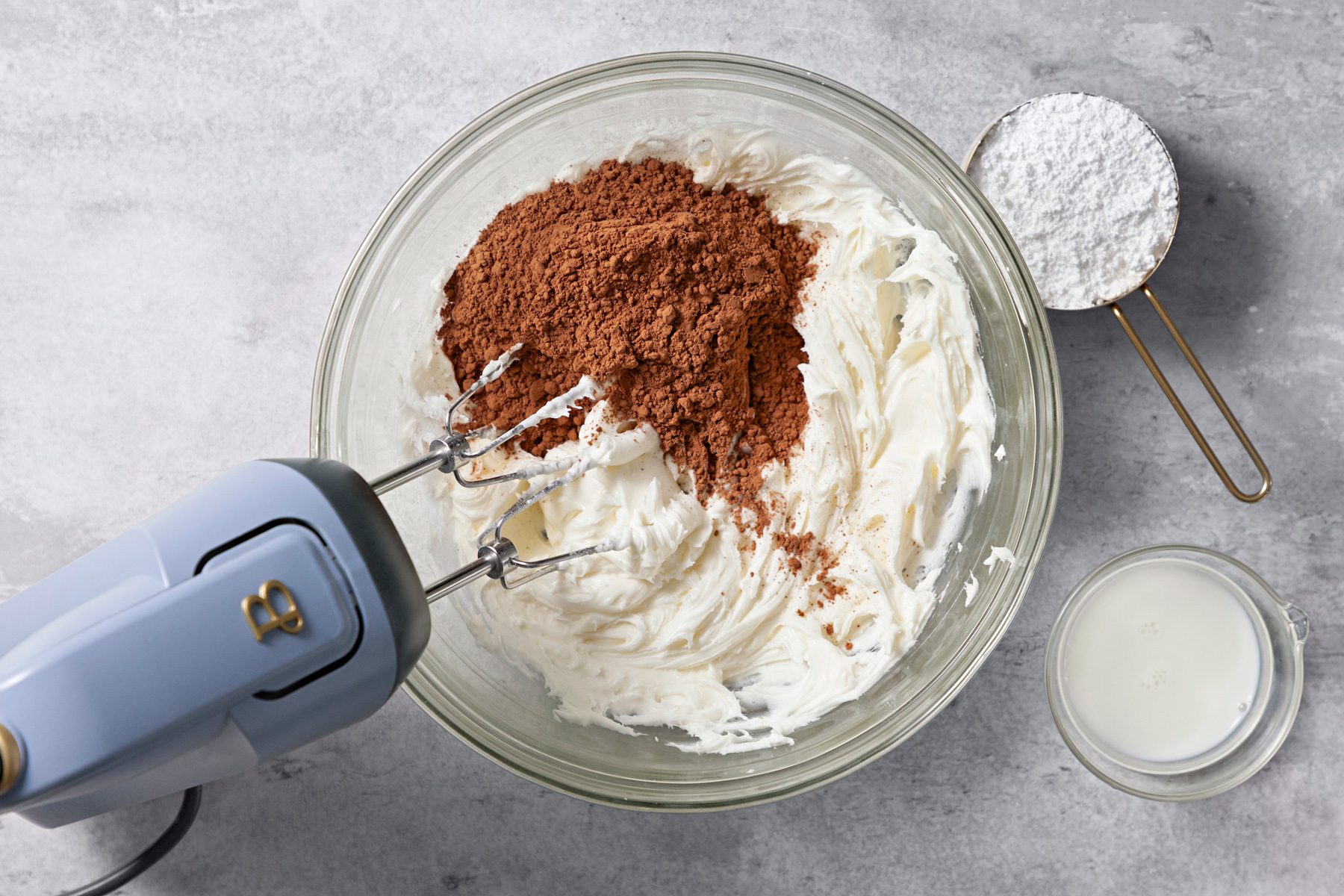 Overhead shot of a large bowl beat butter until light and fluffy; gradually beat in 2 cups confectioners sugar; baking cocoa and milk until smooth; gradually beat in enough remaining powdered sugar to reach desired consistency; blender; grey surface