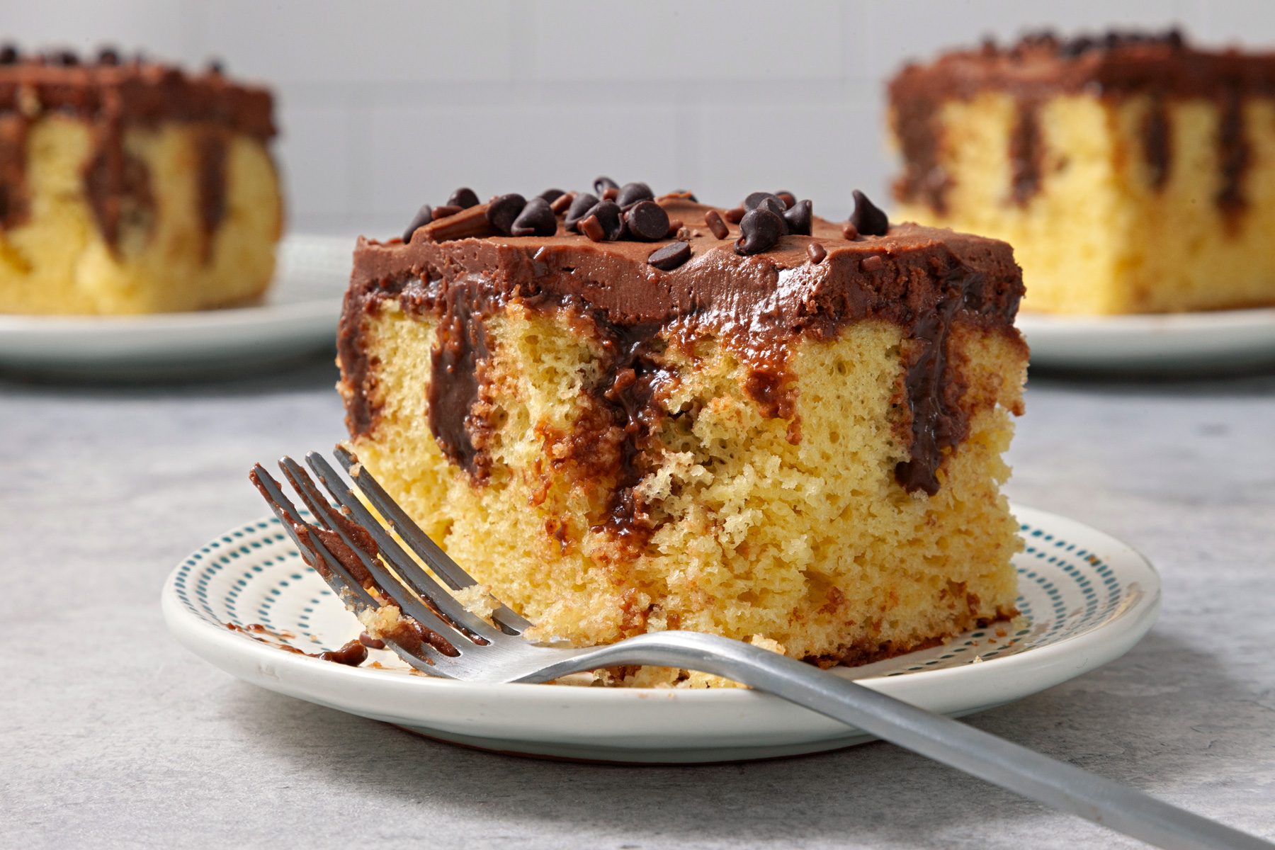 Close shot of Pudding Poke Cake; serve on each plates; garnish with sprinkles and chocolate chips; fork; grey surface