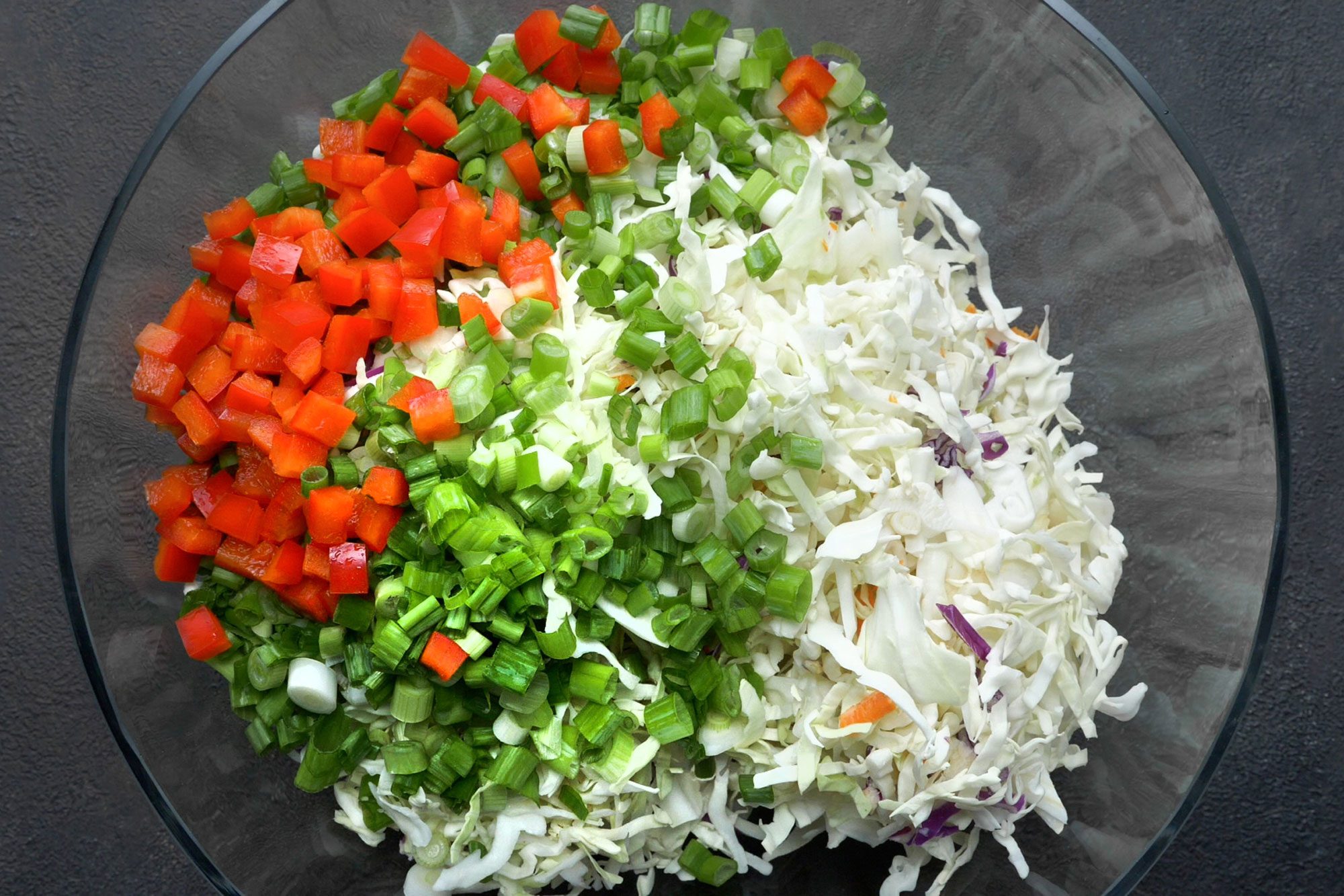 overhead shot; dark grey textured background; In a large bowl, combined coleslaw mix, onions and red pepper;