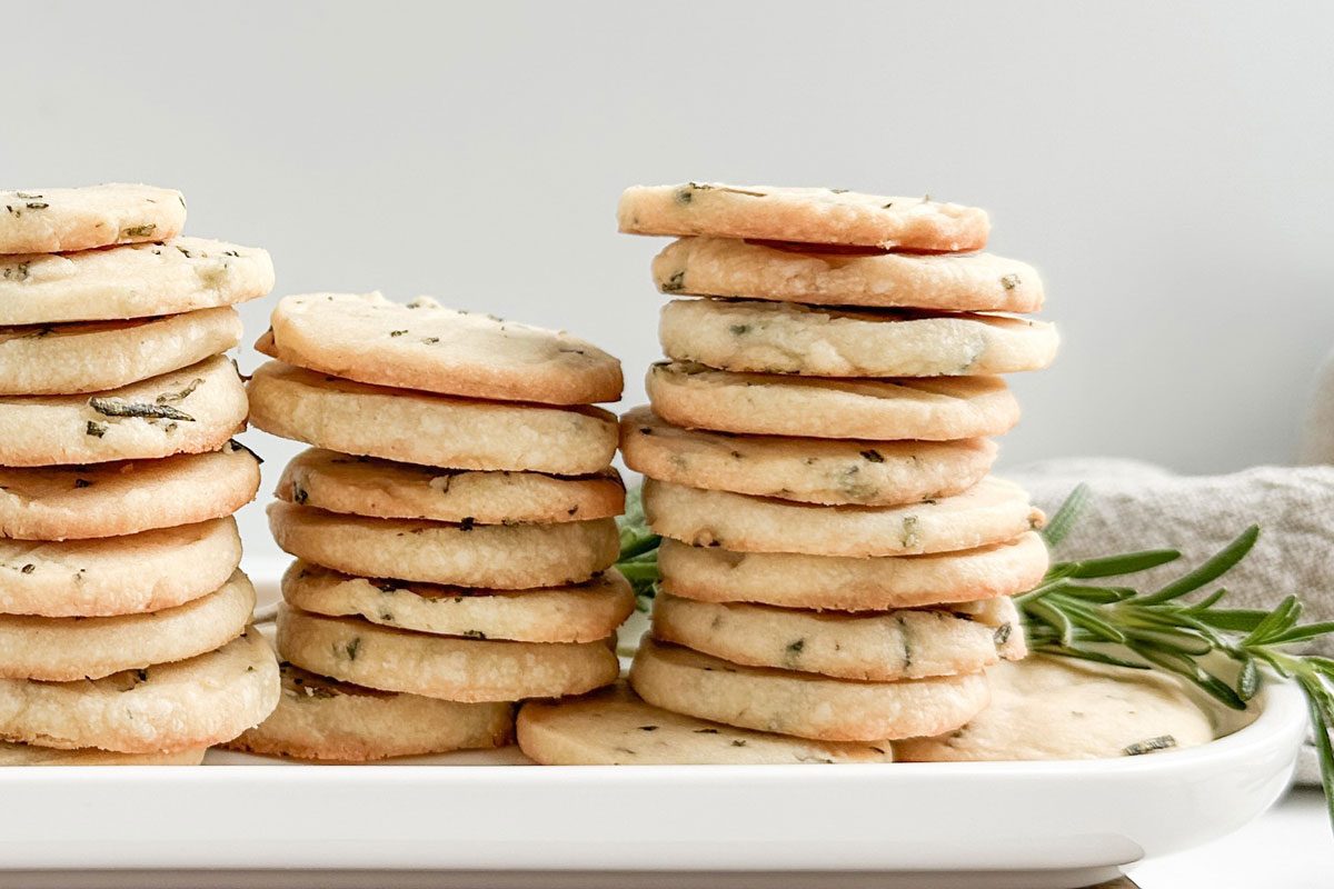 Taste of Home Rosemary Shortbread Cookies on a white tray on a wooden board with sprigs of rosemary