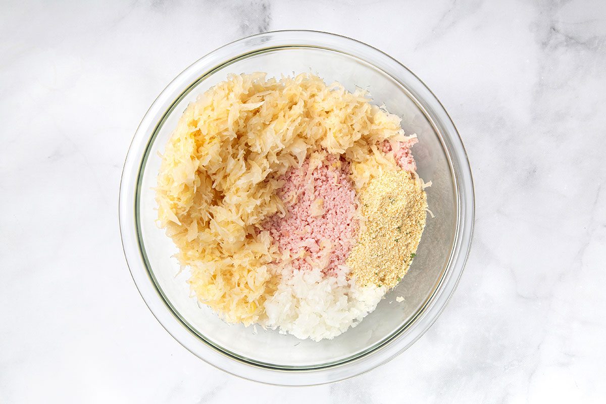 Ground ham, sauerkraut, onion, and breadcrumbs in a mixing bowl for step one of Sauerkraut Balls recipe for Taste of Home