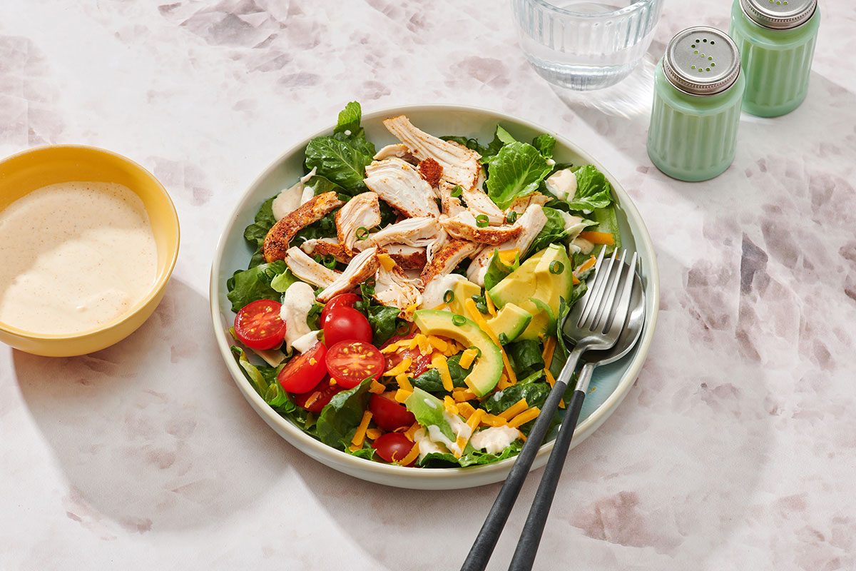 Chicken taco salad assembled on a serving plate with extra salad dressing on the side 
