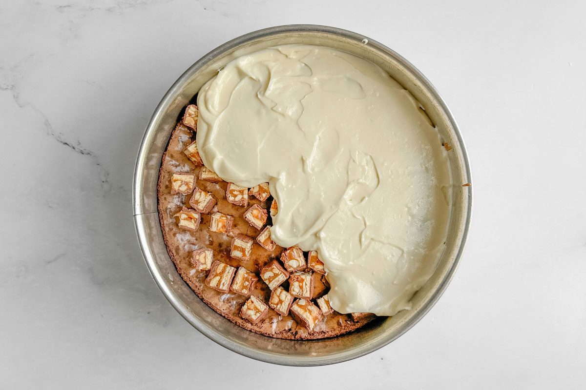 Batter for Taste of Home Snickers Cheesecake in a springform pan on a marble surface