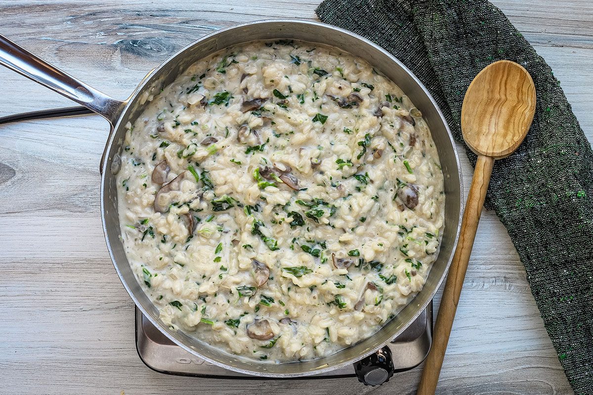 Spinach risotto preparation with cream, mushrooms, spinach, and Parmesan cheese.