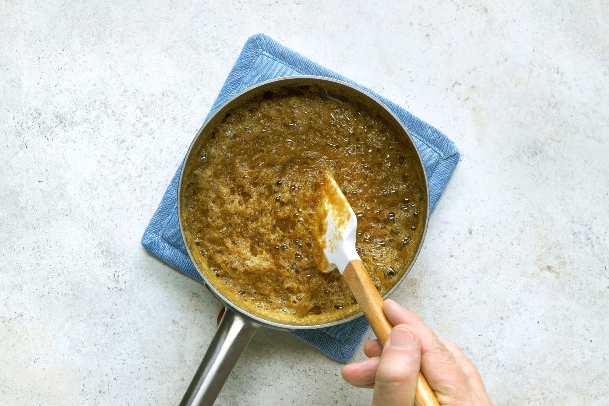 Overhead shot of remove from heat; stir in baking soda; cool to lukewarm; spatula; induction; marble surface;