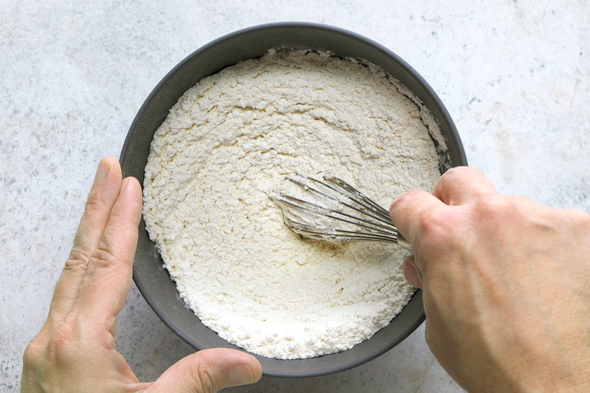 Overhead shot of another bowl; mix flour and baking powder; whisk tool; marble surface;