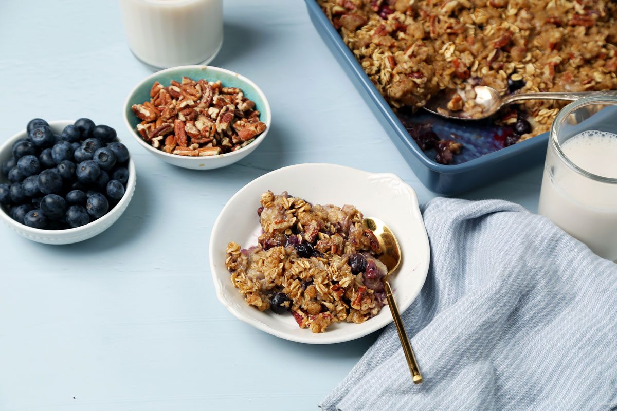 Close up of Taste of Home's Blueberry Baked Oatmeal in a blue baking pan served on a white dish on a light blue surface.