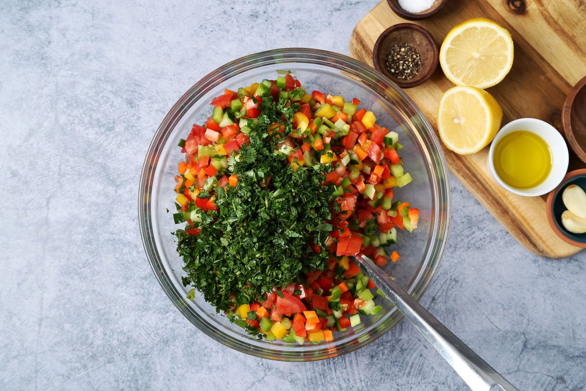 Process of making. Taste of Home's Israeli Salad in a large mixing bowl on a blue surface.