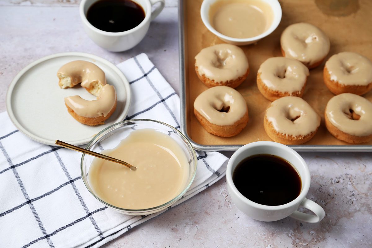 Close up of Taste of Home's Maple Glaze in a bowl with doughnuts on a baking sheet.