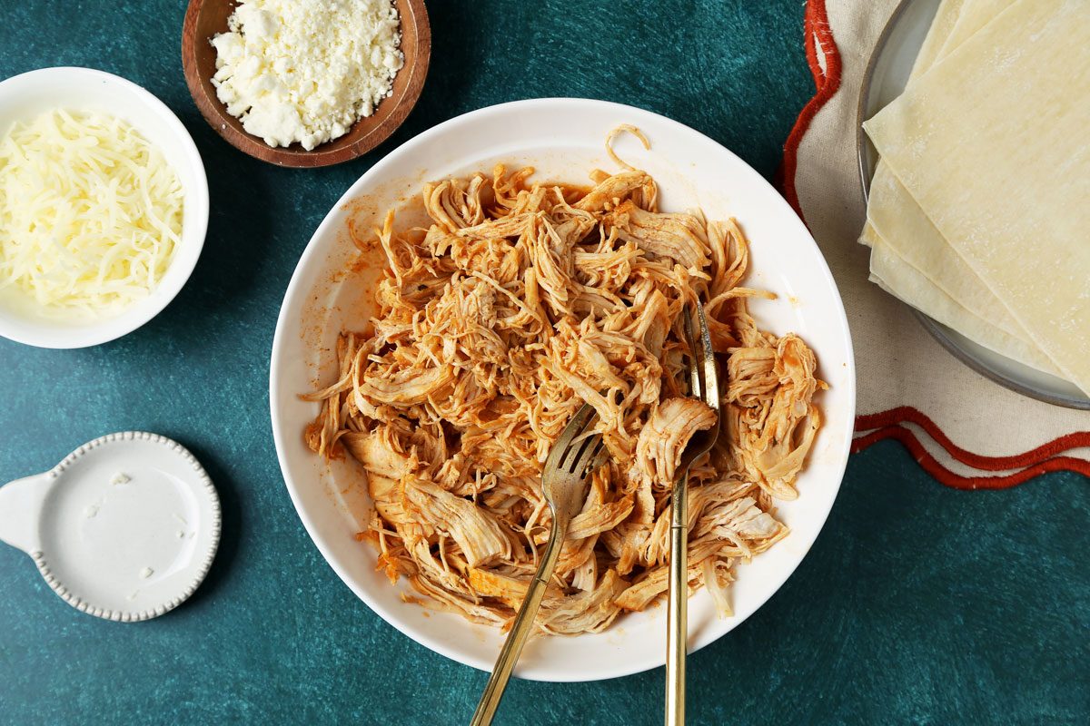 Process of making Taste of Home's Buffalo Chicken Egg Rolls. Buffalo chicken filling in a bowl on a green surface.