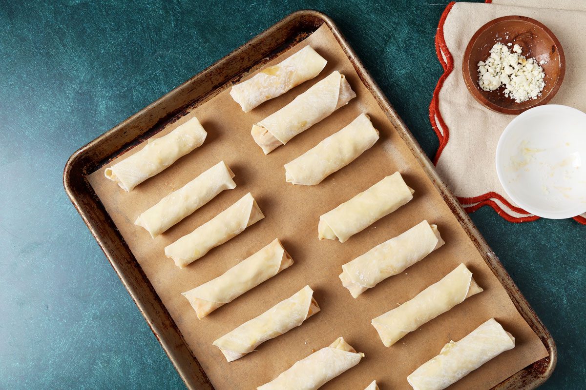 Process of making Taste of Home's Buffalo Chicken Egg Rolls on a baking sheet on a green surface.