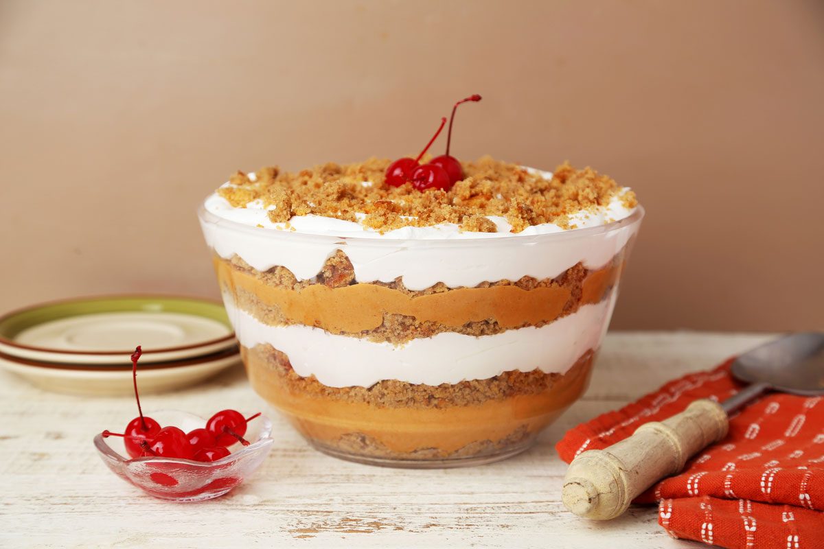 Close up of Taste of Home's Pumpkin Trifle layered in a glass serving bowl on a white wooden surface.