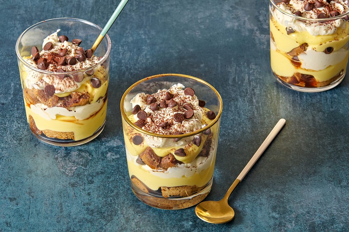 Angled shot of three tiramisu cups being served with spoons
