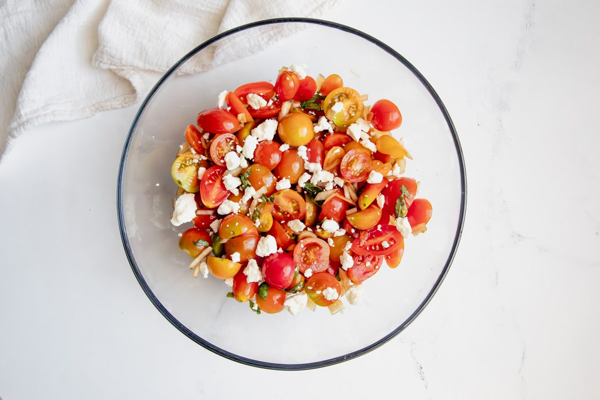 Overhead shot for Taste of Home Tomato Feta Salad with ingredients tossed in a glass bowl topped with feta.