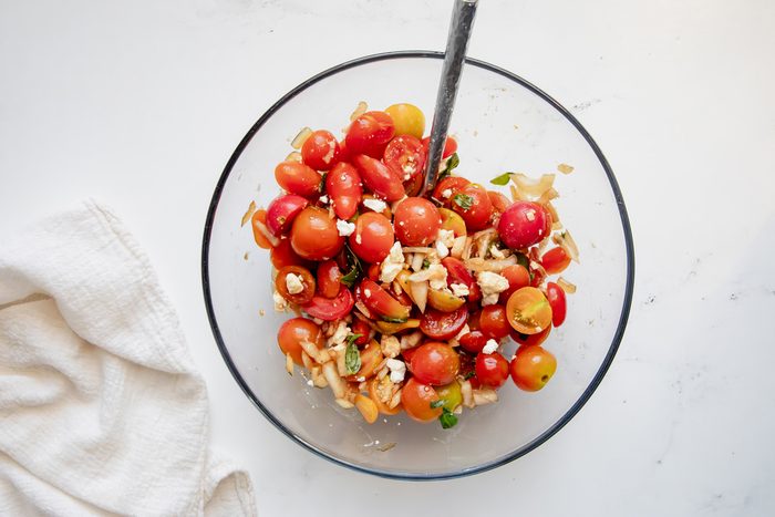 Overhead shot for Taste of Home Tomato Feta Salad with ingredients tossed in a glass bowl topped with feta with a spoon.