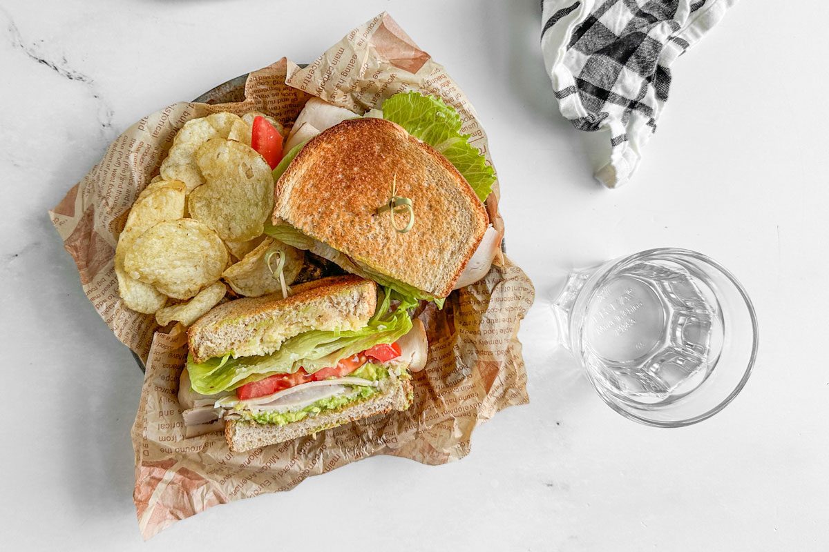 Taste of Home Turkey Avocado Sandwich on a parchment lined metal plate with potato chips