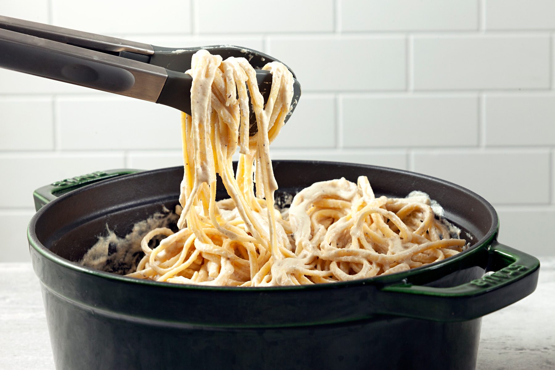Table view shot of pot; top with additional pepper; tongs; white bricks wall background