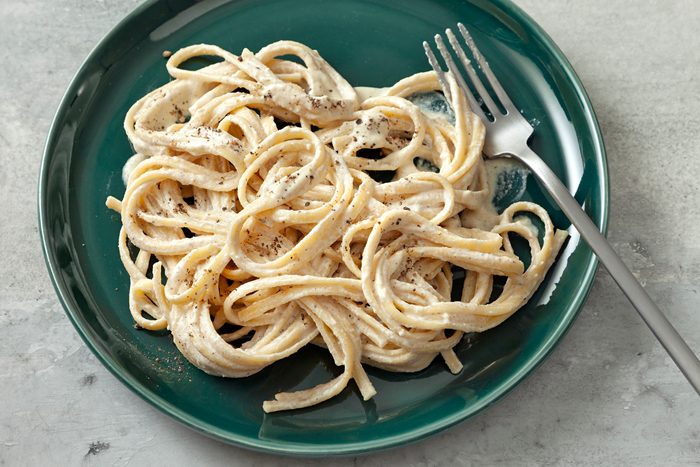 High angle view shot of Vegan Alfredo Sauce; serve with pasta; top with additional pepper; fork; grey marble surface