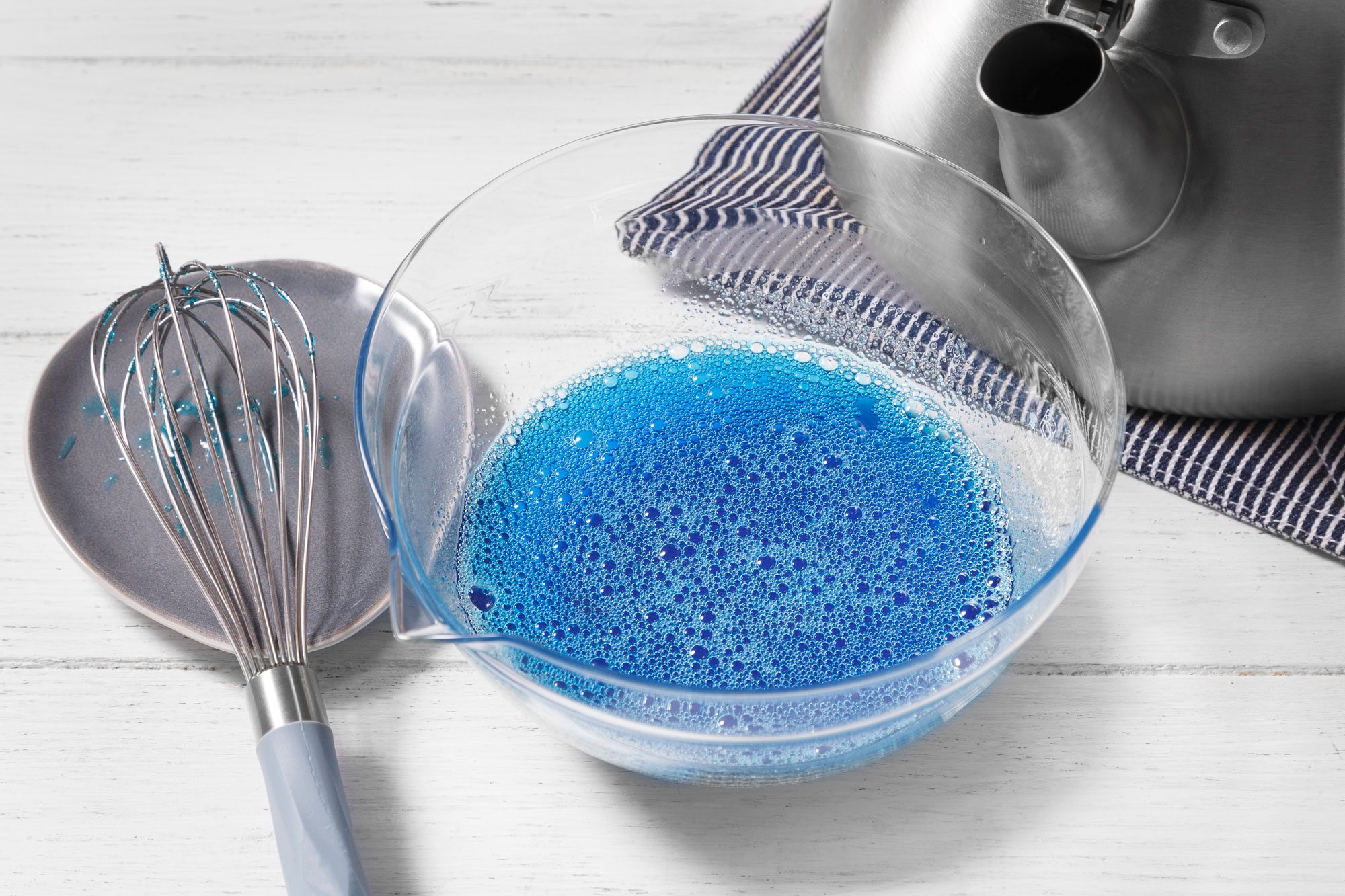 A clear glass bowl sits on a white wood table and it is filled with blue liquid