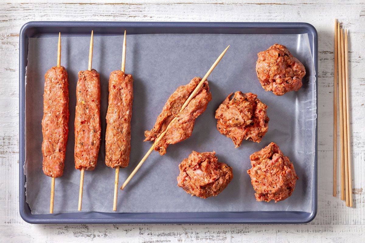 Divided meat mixture is being shaped into rectangles around skewers