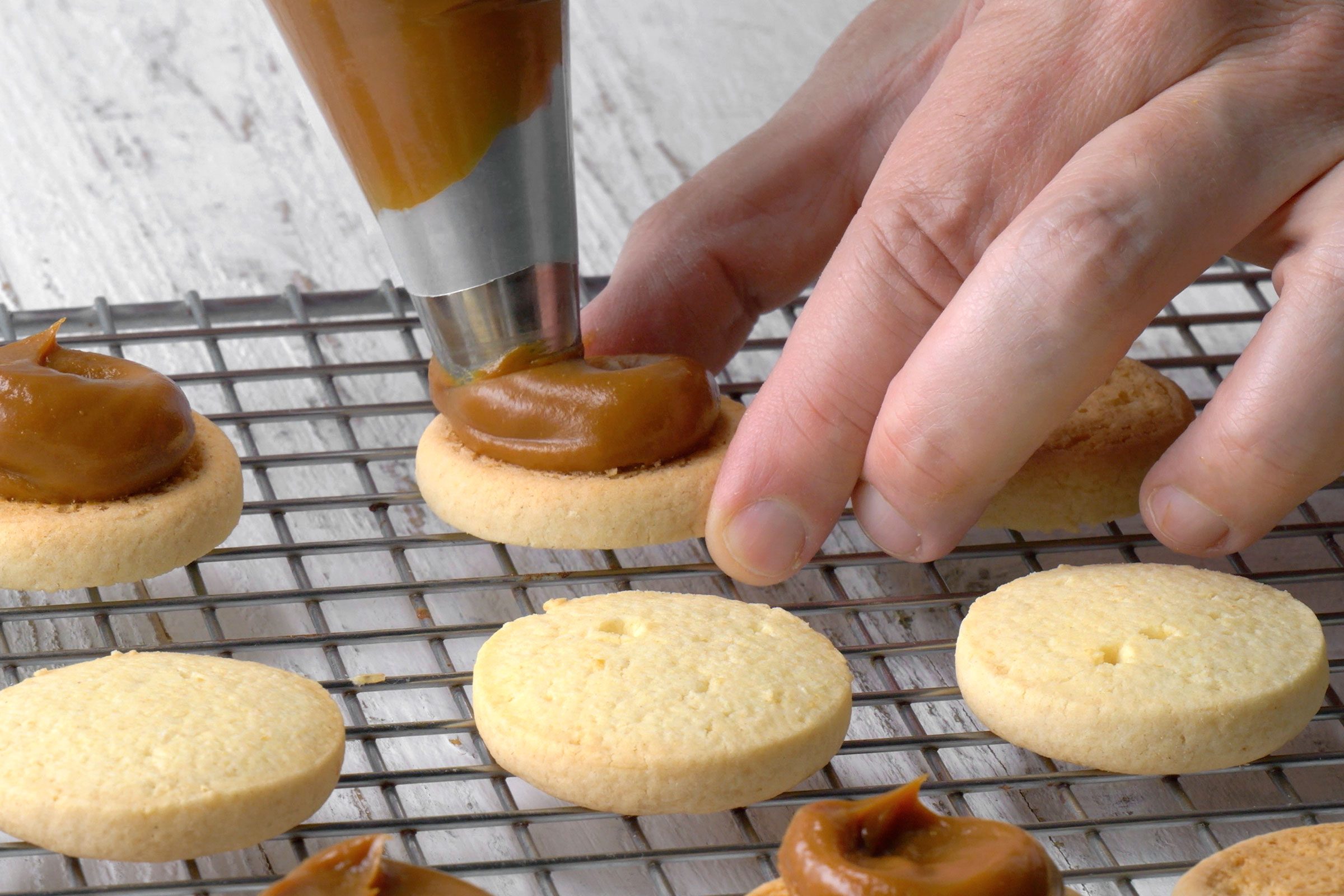 Piping a thick layer of dulce de leche in a swirling motion on the flat side of half of the cookies