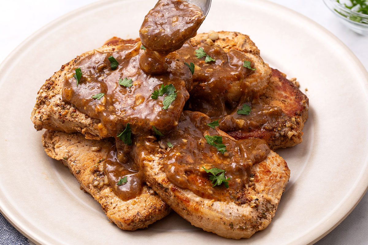 Apple Cider Pork Chops topped with parsley on a serving platter for Taste of Home