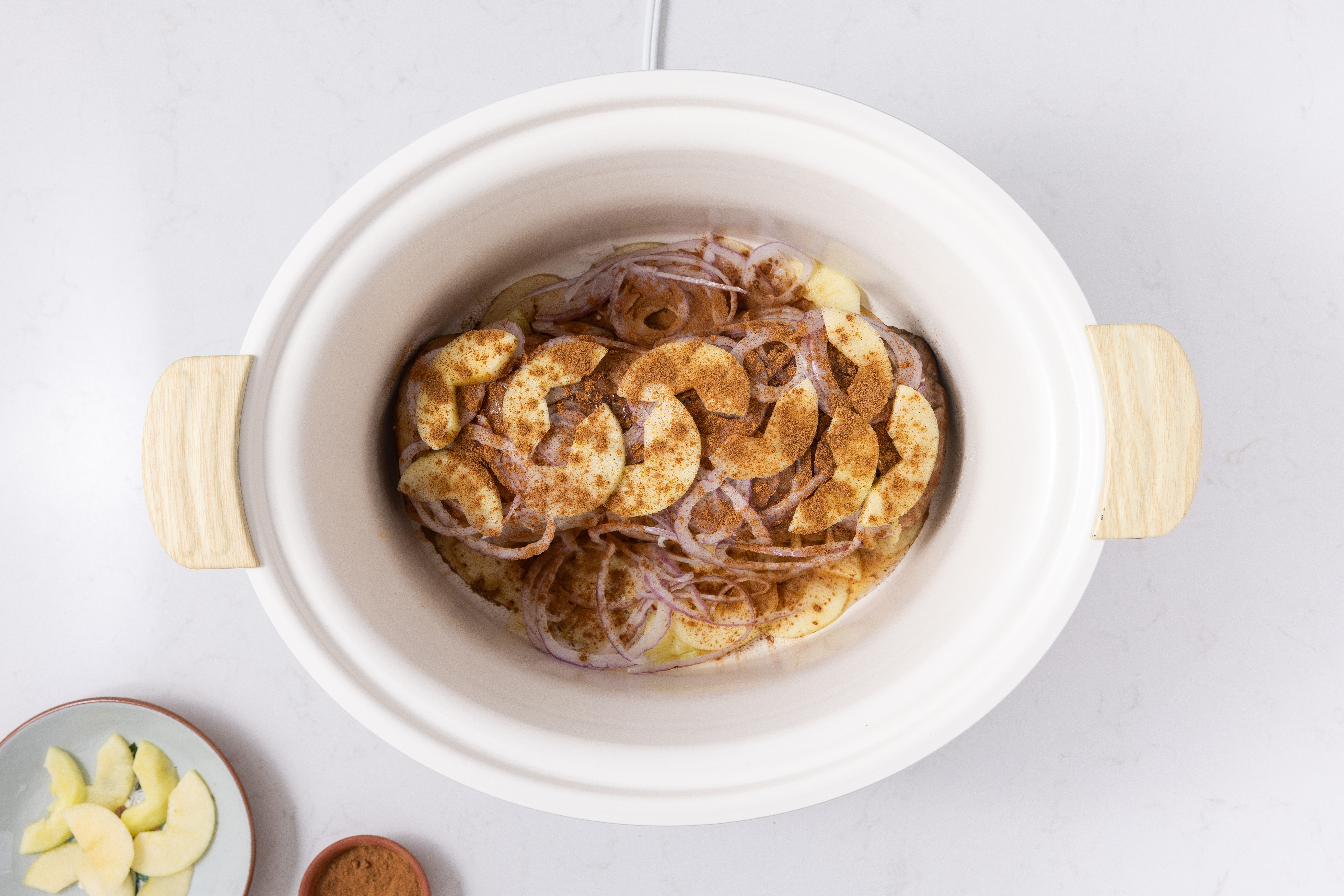 Pork loin on slow cooker topped with red onions, apple slices and cinnamon.