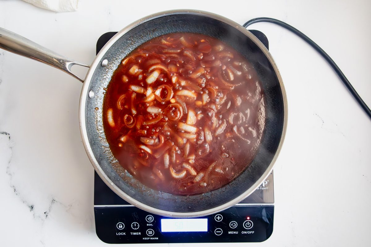 Overhead shot for Taste of Home Apple Chicken with sauce cooking over an induction cooktop.