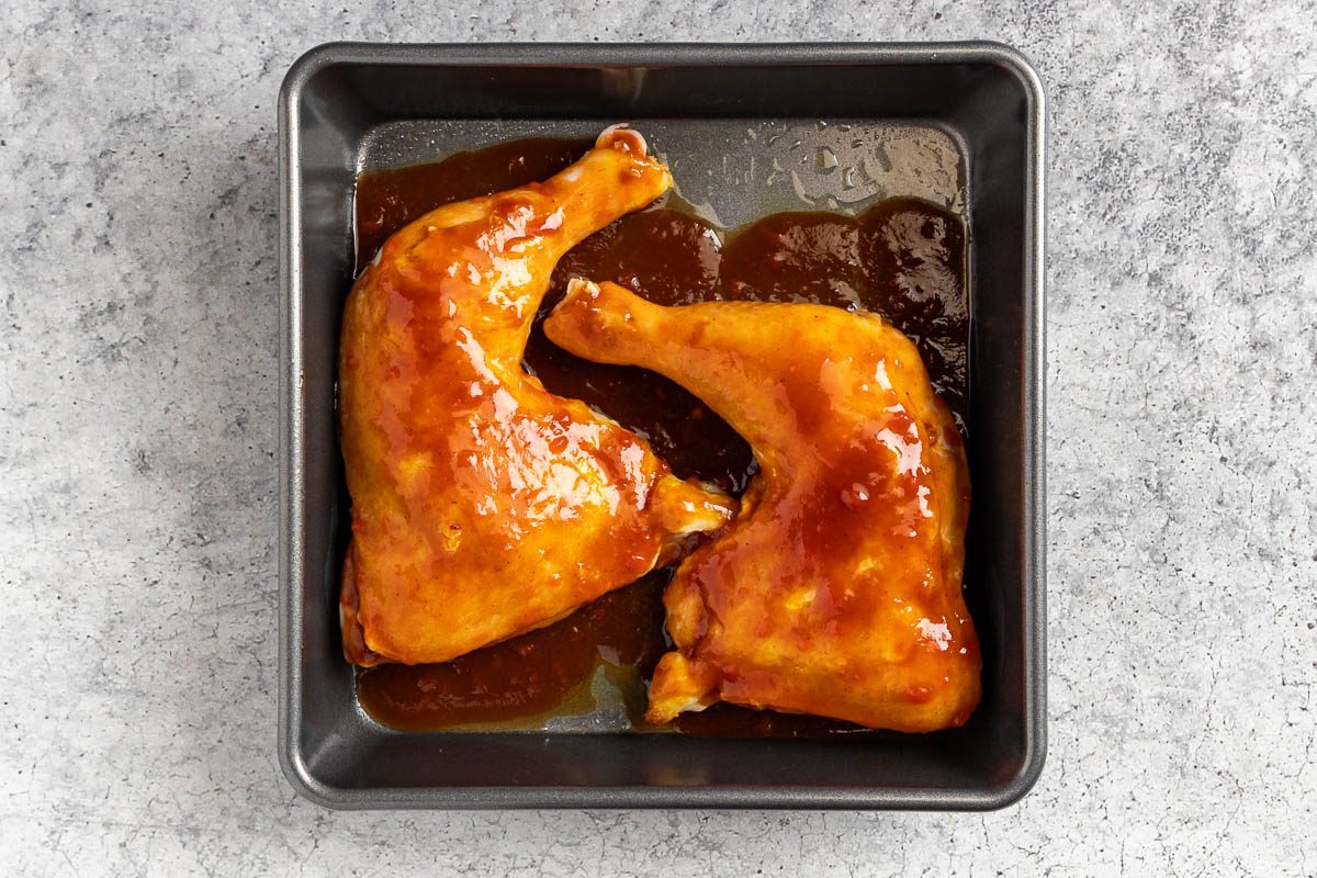chicken covered with the bbq sauce in a baking pan.
