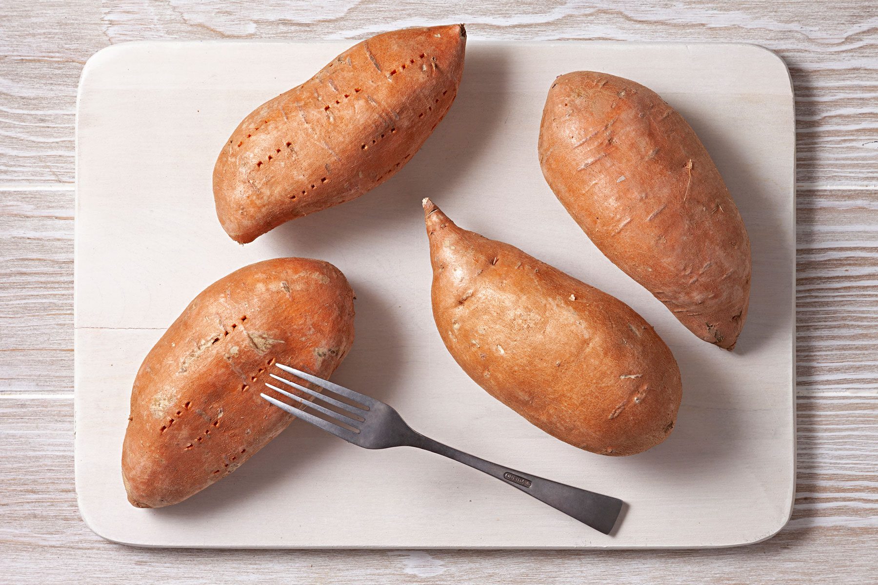 Sweet potatoes on baking sheet. One potato has a fork in it.