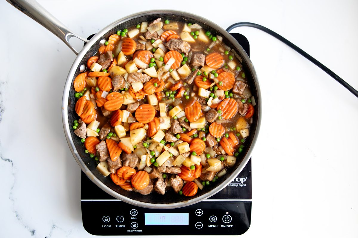 Overhead shot for Taste of Home Beef Potpie with Biscuits, ingredients cooking over an induction cooktop.