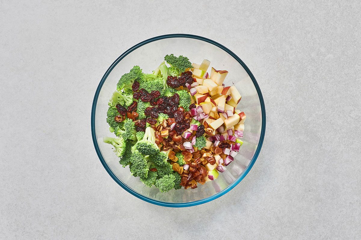 Broccoli apples dried fruits and onion combined in a large bow