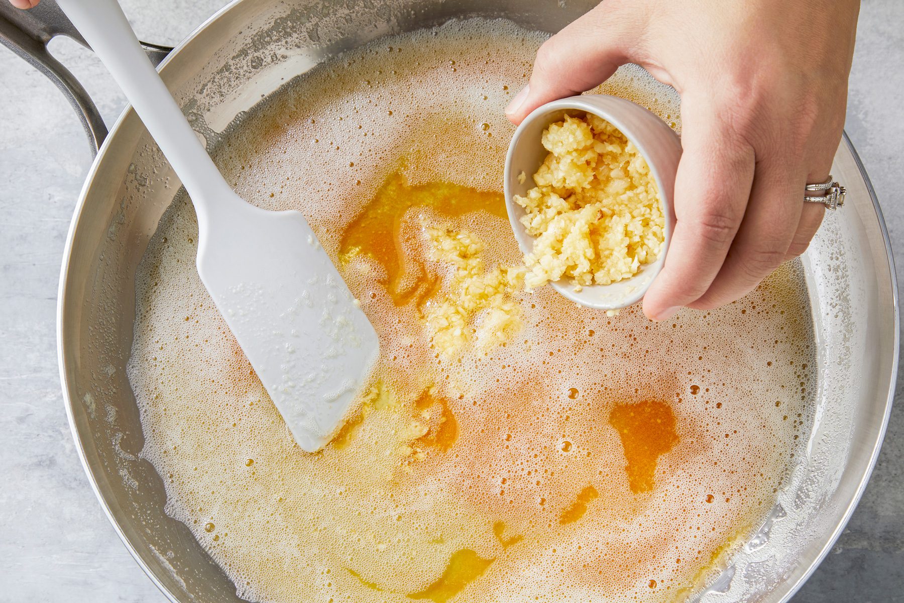 A close-up of the golden brown butter in the saucepan, with minced garlic being added just before the cooking time ends.