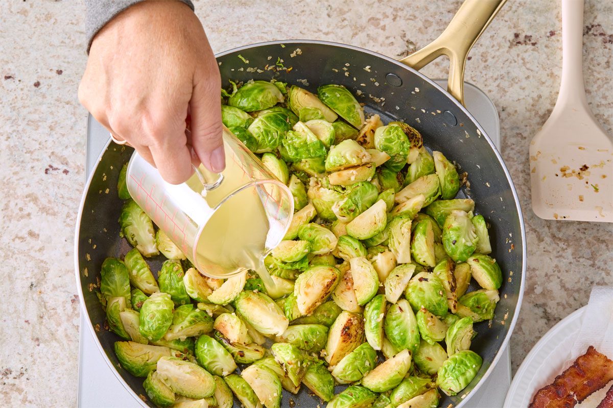 Overhead shot of add 1/2 cup chicken broth; bring to a simmer; cook until evaporated; 2-3 minutes; stirring occasionally; marble surface;