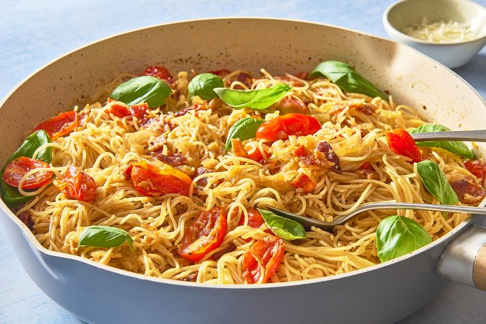 Closeup shot of caramelised onion pasta in a skillet being served with utensils