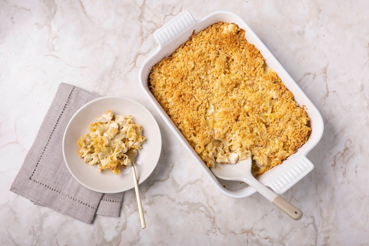 Single serving of Chicken Noodle Casserole in a bowl next to the whole dish overhead view on a marble table