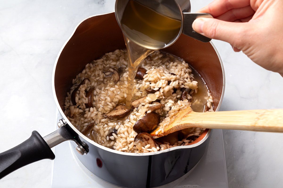 Chicken broth added to rice mixture in a saucepan for step four of Chicken Risotto recipe for Taste of Home