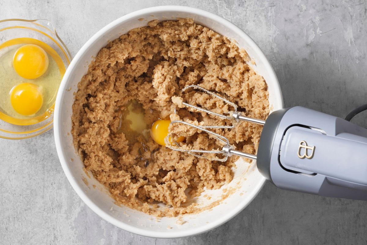 Adding eggs into creamed butter and brown sugar mixture in a mixing bowl