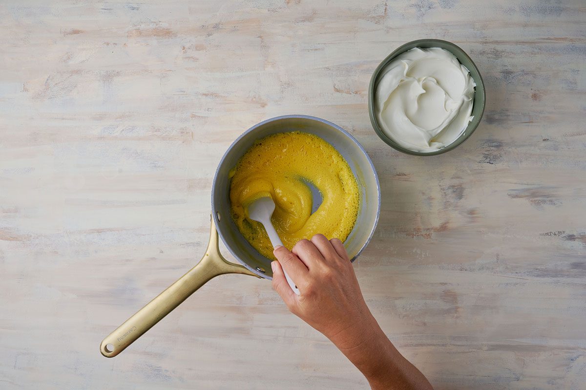 Preparing the Dressing for Christmas Fruit Salad. A saucepan filled with a mixture of egg yolks, water, vinegar, and salt being stirred over medium heat.